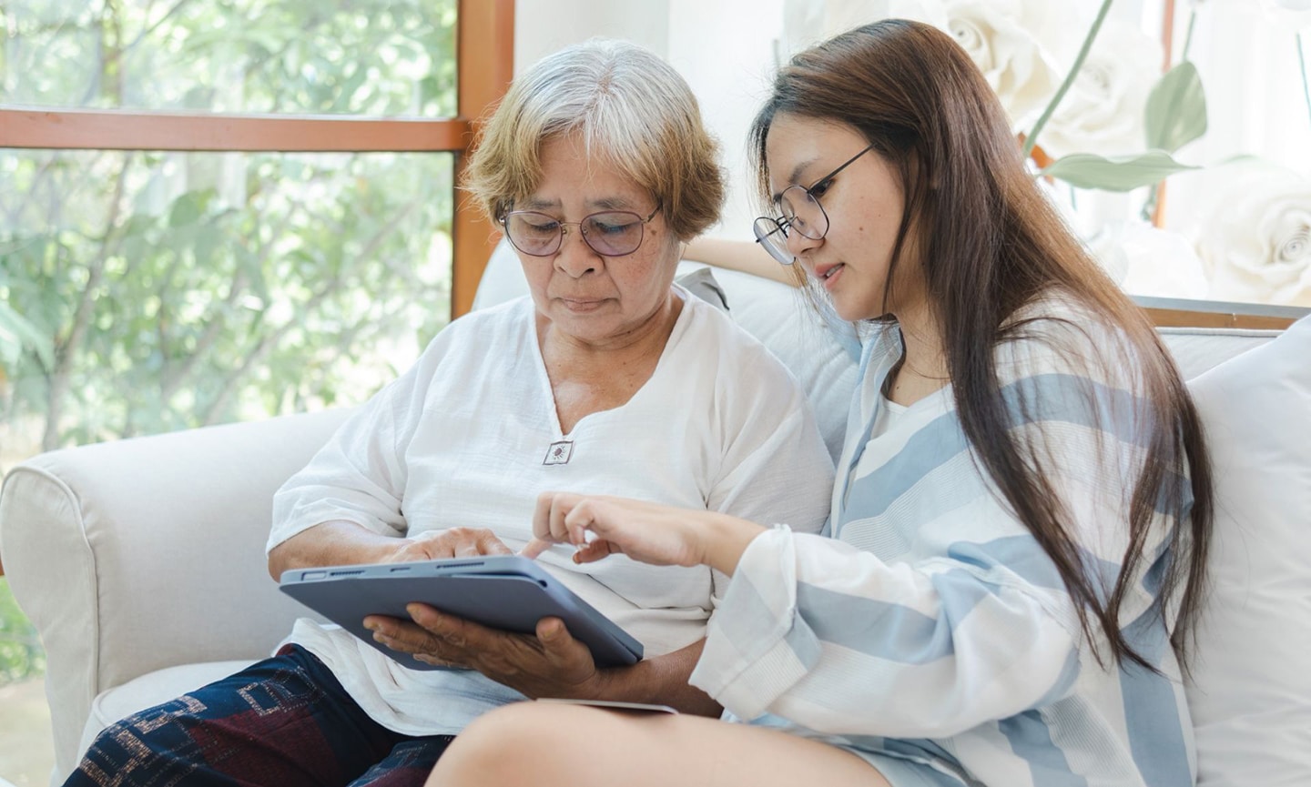 Senior person and adult family-member sit together while looking at a tablet