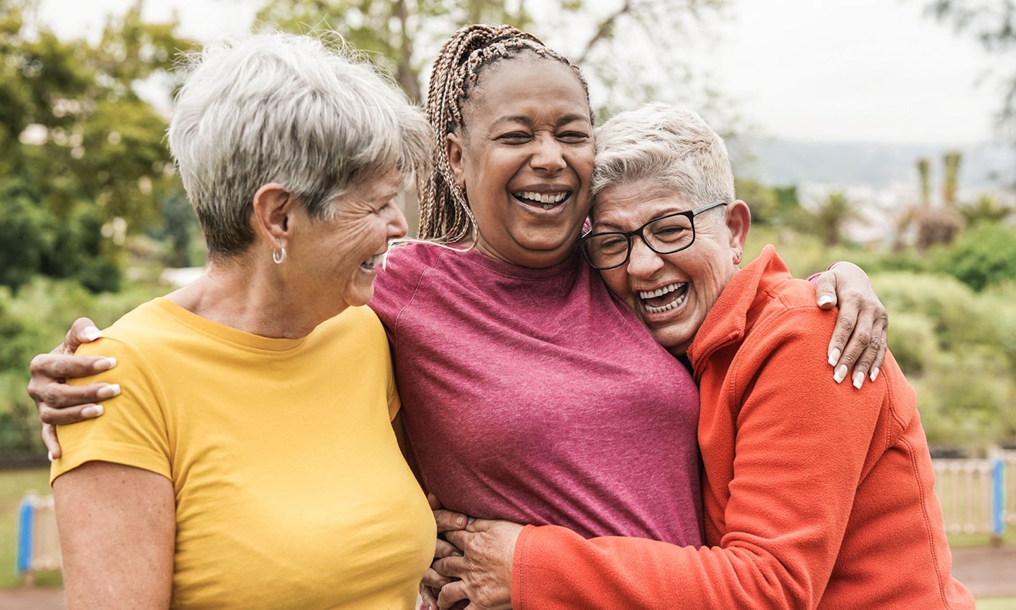 A group of Medicare aged women hugging eachother at a park