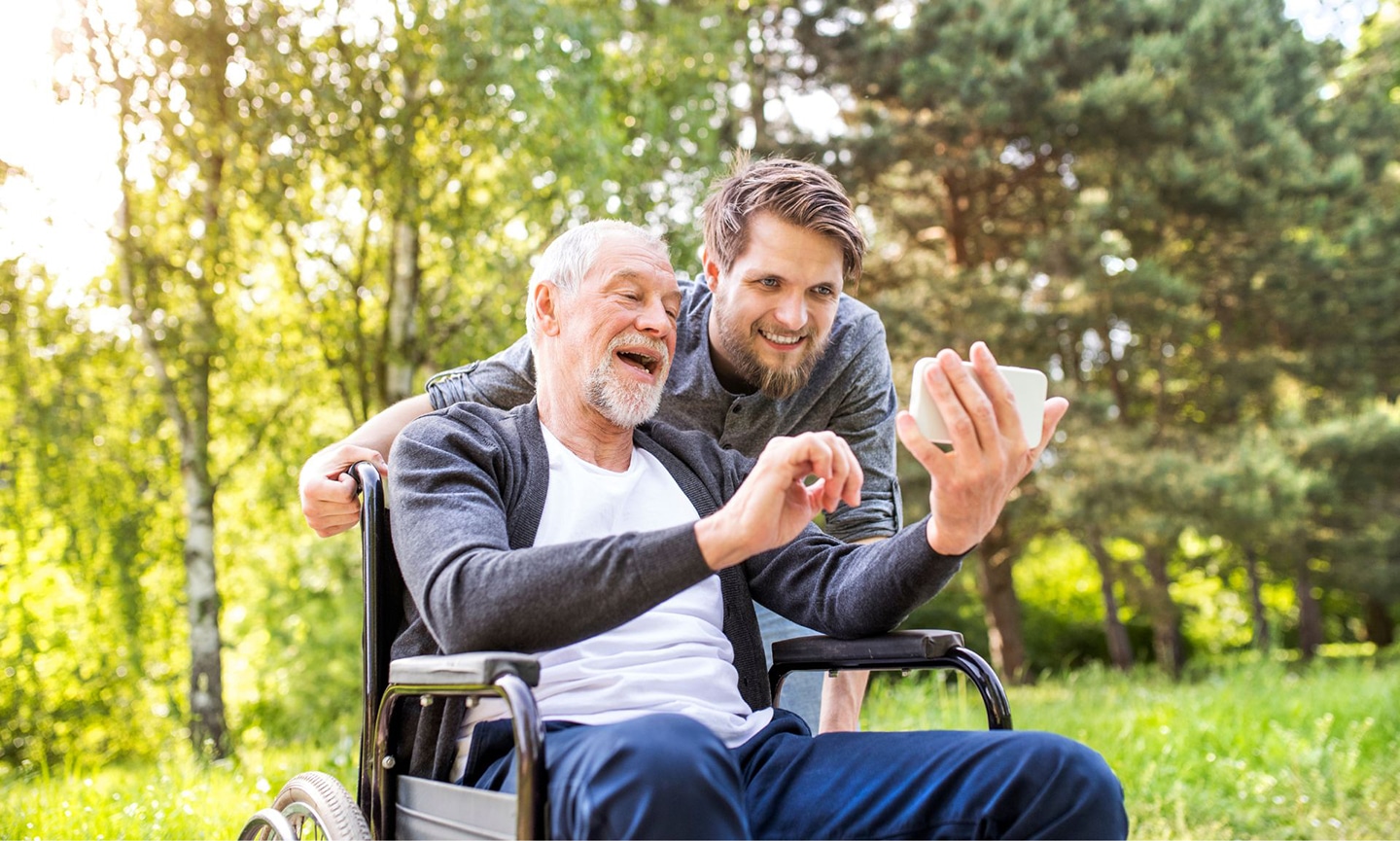 Elderly man in wheelchair takes a selfie with adult son while on a walk in Colorado