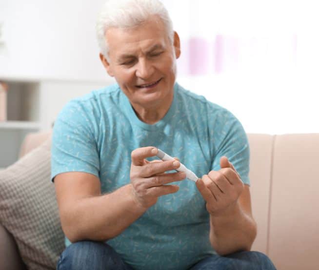 A person sits at home using a lancet to test their blood glucose levels using an at-home monitor.