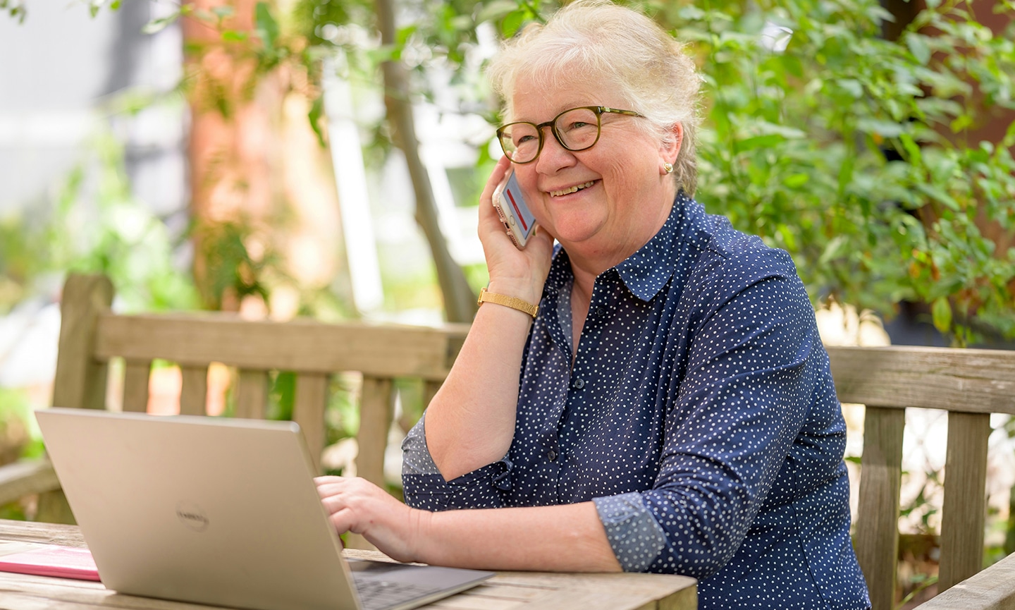 Female smiling while talking on a phone and using a laptop.